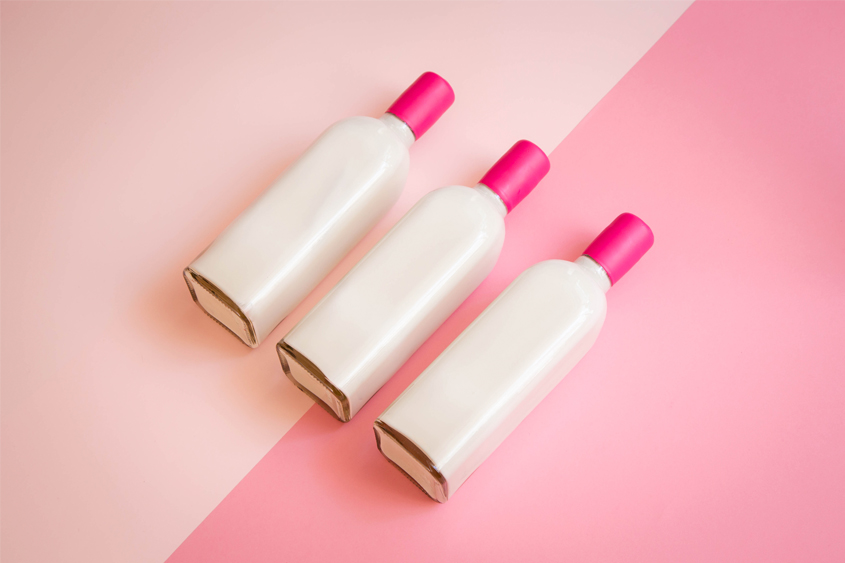 Botella color blanca con lacre color magenta en el cuello de la botella y un fondo bicolor de dos tonalidades de rosa