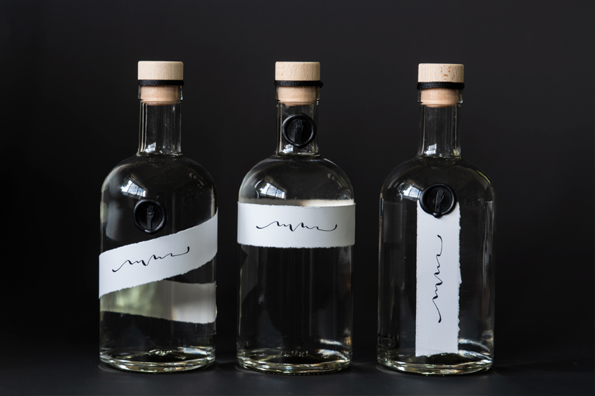 Tres botellas con tequila cristalino con medallón de lacre color negro con diseño de mano