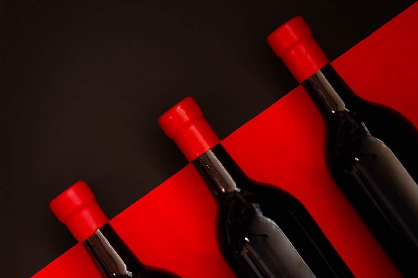 Botellas color negro en fondo rojo, y lacre rojo en el cuello de las botellas en un fondo negro, acomodadas en diagonal