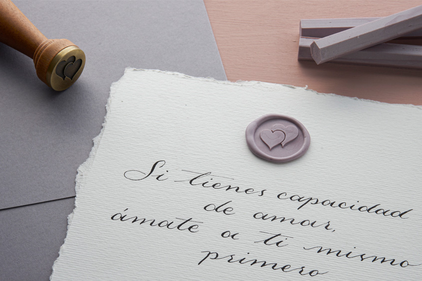 Carta escrita en caligrafía, acompañada por un medallón del diseño de corazones en color lavanda, barras de lacre lavanda y el sello