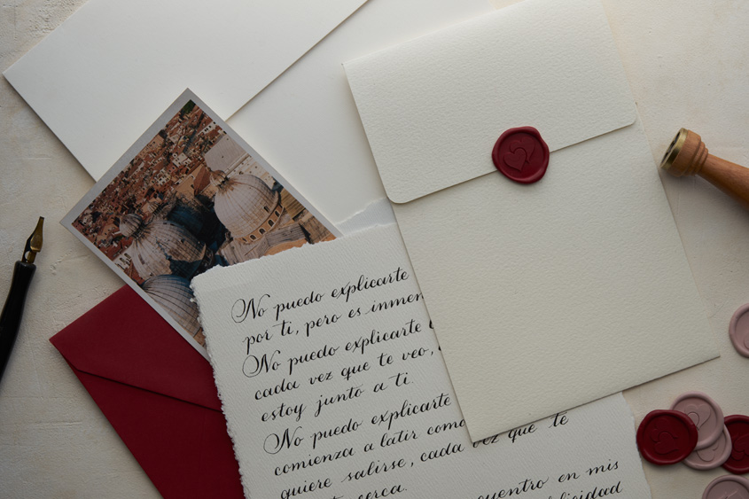 Carta escrita en caligrafía, acompañada por un medallón del diseño de corazones en color rojo, medallones de lacre rojo y lavanda
