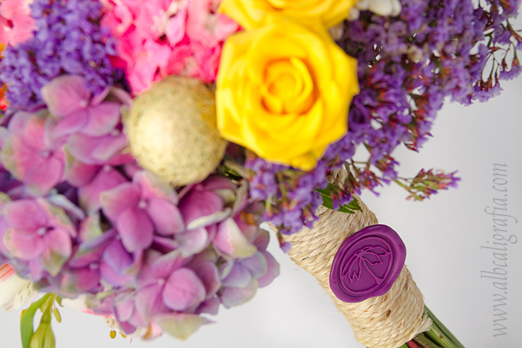 Ramo de flores en colores en tonos amarillos, rosa y morado atado y sellado con un medallón de lacre morado