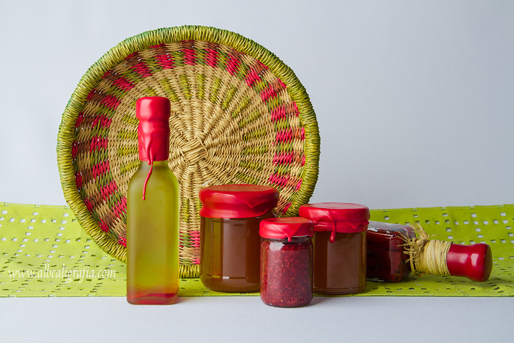 Botellas de aceite y de conservas lacradas en color rojo, decorados con un canasto de mimbre y una tela verde