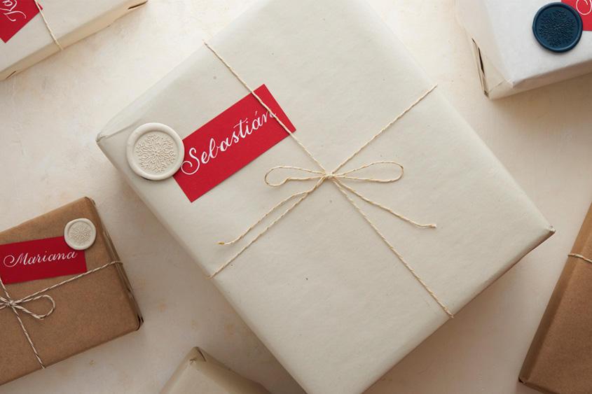 Caja de regalo con letrero rojo escrito en caligrafía el nombre de Sebastián, y un medallón de lacre marfil con diseño de copo de nieve