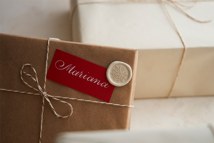 Caja de regalo con letrero rojo escrito en caligrafía el nombre de Mariana, y un medallón de lacre marfil con diseño de copo de nieve
