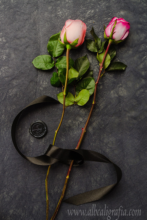 Un par de rosas rosas unidas con un listón y un medallón de lacre color negro 