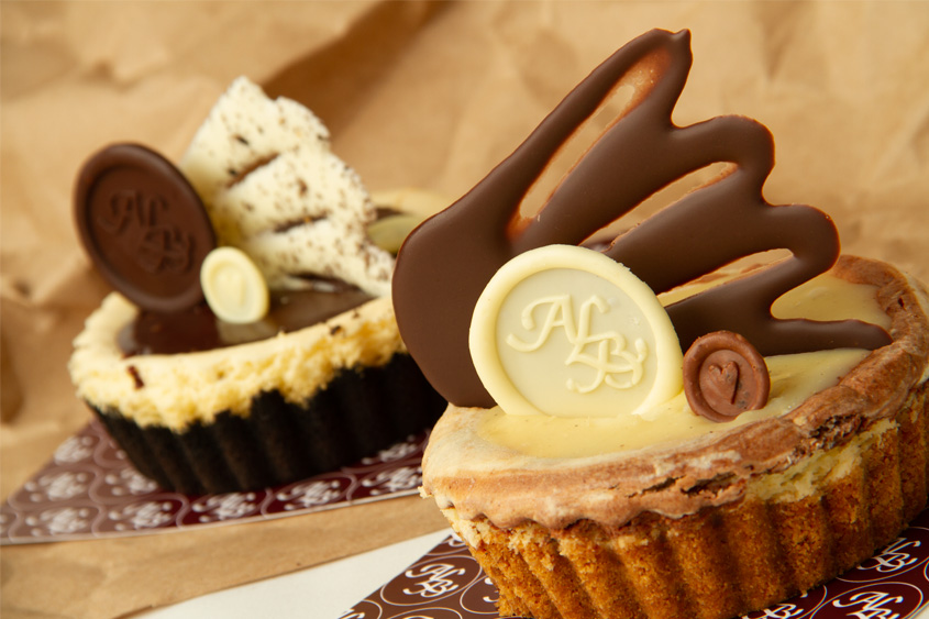Medallón de chocolate hecho con sello metálico con el logo de ALB y corazón decorando dos pasteles individuales.