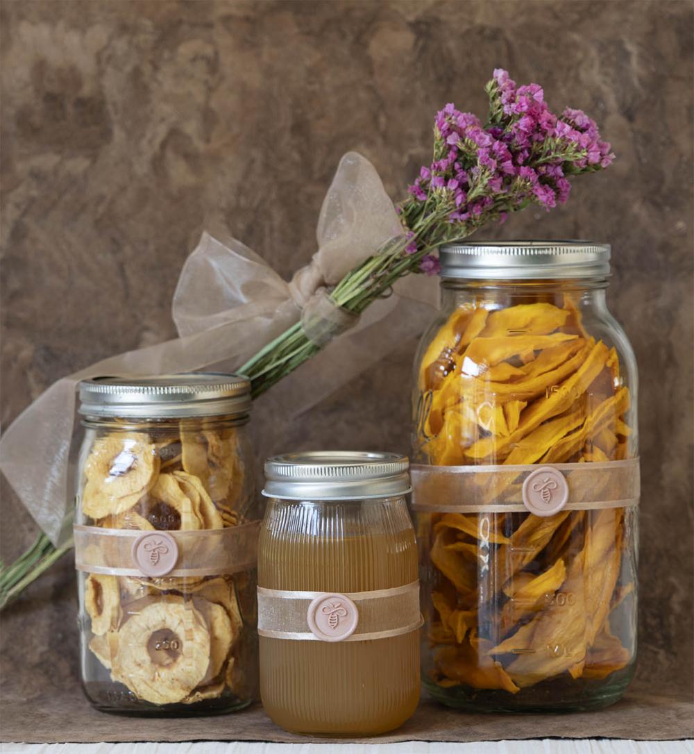 Frascos de cristal con fruta deshidratada y miel en su interior, decorados con un listón color beige y un medallón de lacre con digura de abeja en col