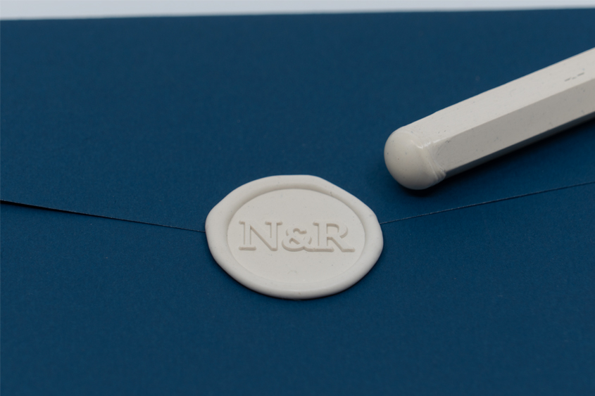 Sobre azul lacrado con sello con iniciales N&R en color marfil, junto con una barra de lacre para papel un poco derretida de la punta