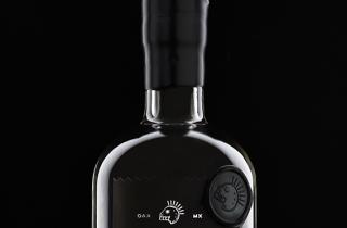 Botella de Tumba 7 Mezcal, con nuestro lacre negro en el cuello de la botella y un medallón de lacre con su logo pegado en la parte superior derecha d