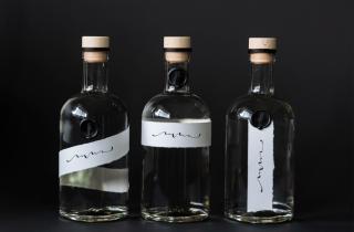 Tres botellas con tequila cristalino con medallón de lacre color negro con diseño de mano