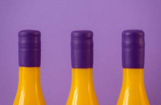 Tres botellas color amarillo en fondo color lila, y lacre morado en el cuello de las botellas