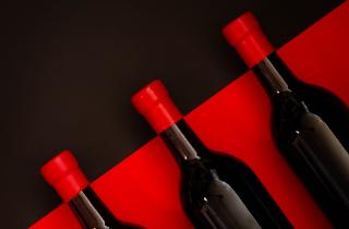 Botellas color negro en fondo rojo, y lacre rojo en el cuello de las botellas en un fondo negro, acomodadas en diagonal