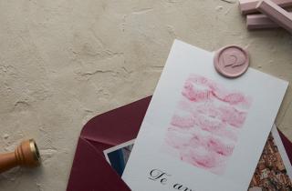 postal escrita en caligrafía la palabra Te Amo, acompañada por un medallón del diseño de corazones en color rosa, barras de lacre rosas y el sello