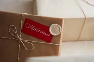 Caja de regalo con letrero rojo escrito en caligrafía el nombre de Mariana, y un medallón de lacre marfil con diseño de copo de nieve